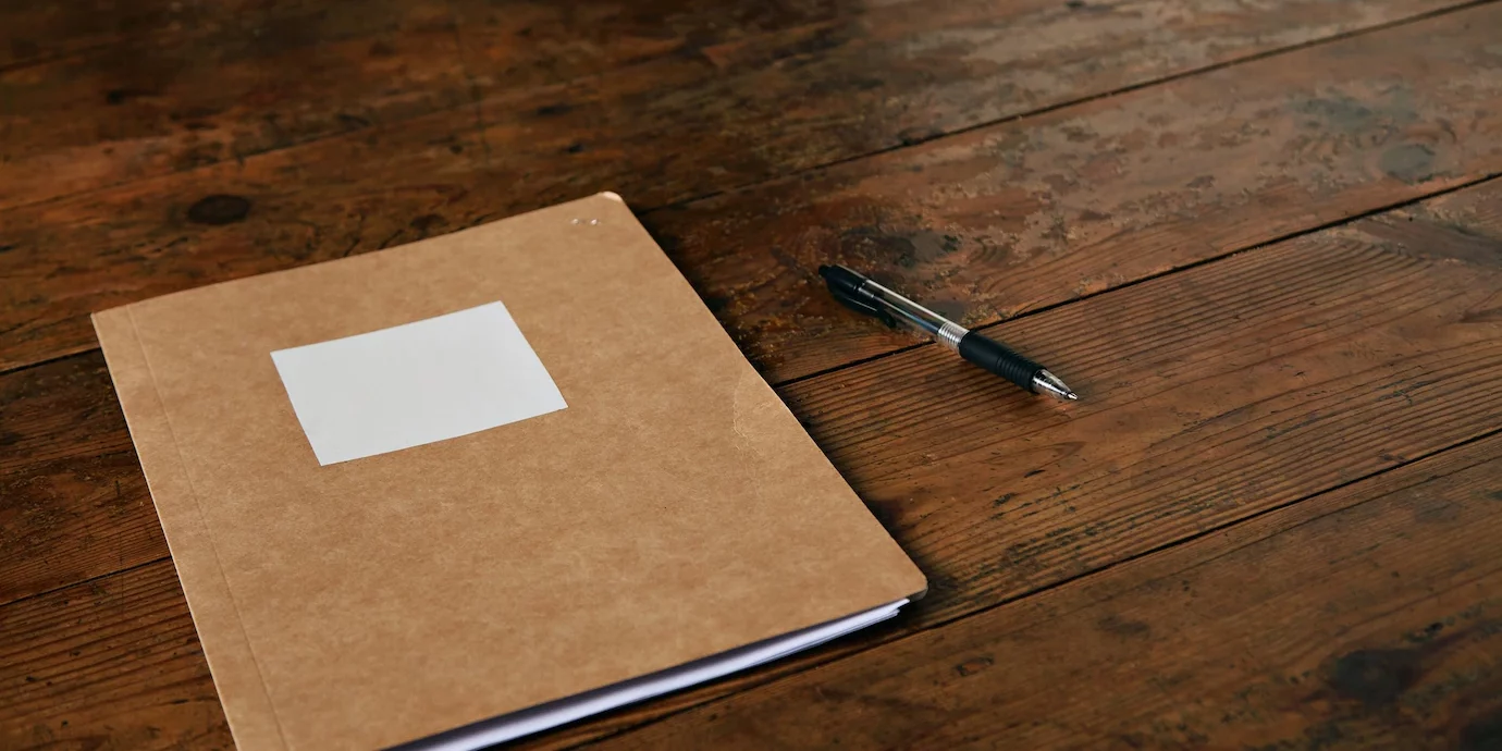 craft-dossier-marron-etiquette-blanche-vide-stylo-bille-table-brun-fonce-rustique_346278-393